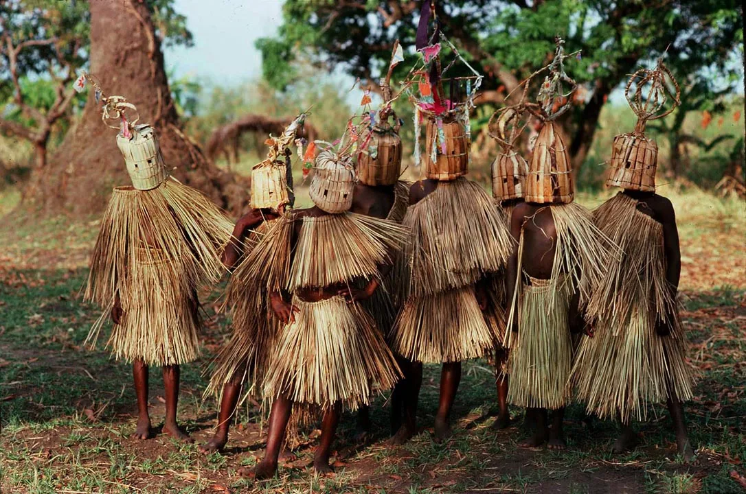Des initiés masqués en costumes de paille se tiennent alignés sous les arbres lors d'un rituel d'initiation au Malawi.