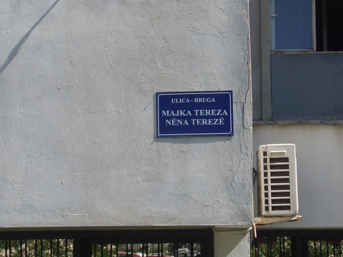 Une plaque de rue bilingue en albanais et en serbe fixée sur le mur clair d'un bâtiment à Ulcinj, au Monténégro.